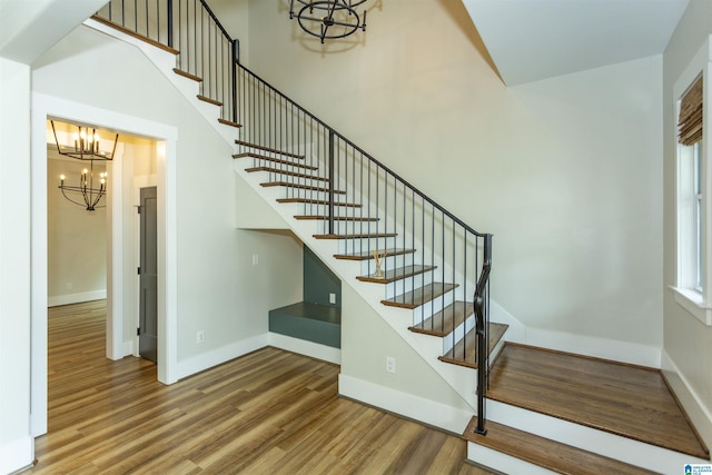 staircase featuring baseboards, wood finished floors, and a chandelier
