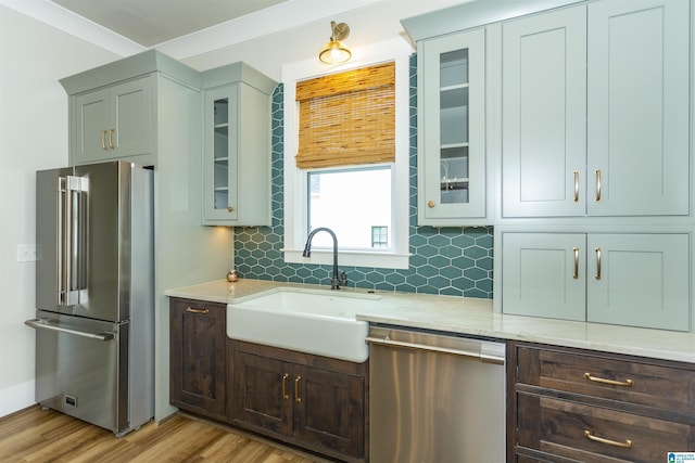 kitchen featuring a sink, light wood-style flooring, stainless steel appliances, tasteful backsplash, and glass insert cabinets