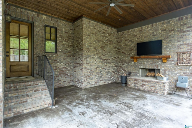 unfurnished living room with ceiling fan, brick wall, stairway, wooden ceiling, and an outdoor brick fireplace