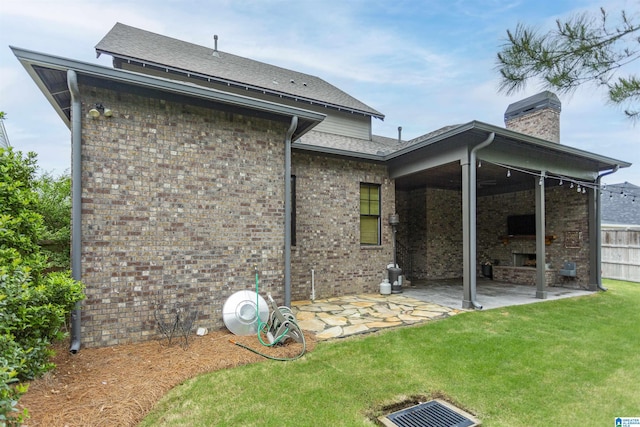 back of property with a chimney, an outdoor fireplace, brick siding, a yard, and a patio