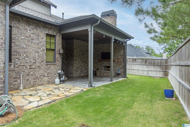 view of yard with an outdoor stone fireplace, a patio, and a fenced backyard