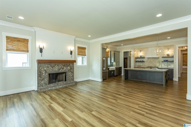 unfurnished living room featuring an inviting chandelier, ornamental molding, a wealth of natural light, and wood finished floors