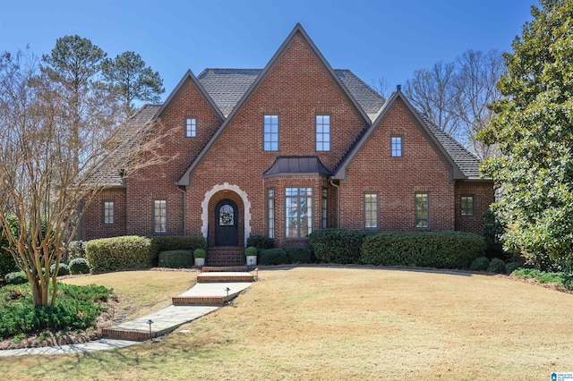 tudor home with brick siding, a shingled roof, a front lawn, and a standing seam roof