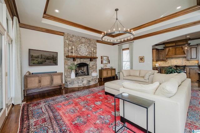 living area with dark wood-style flooring, a stone fireplace, crown molding, a notable chandelier, and a tray ceiling