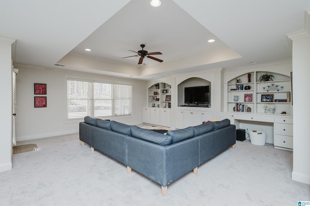 living area with crown molding, a raised ceiling, built in shelves, carpet, and a ceiling fan