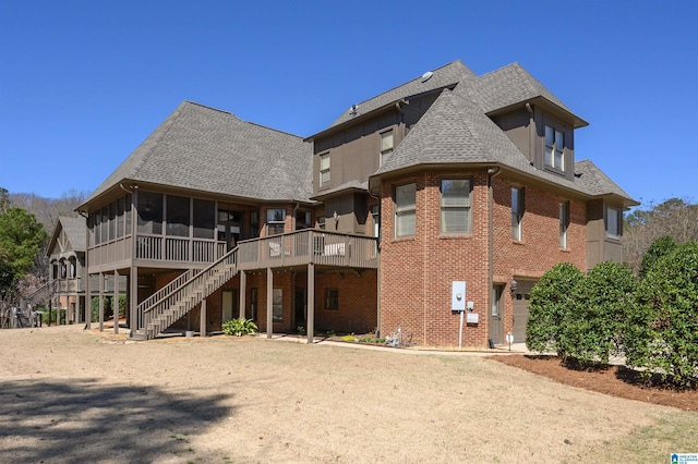 rear view of house featuring roof with shingles, a deck, a sunroom, stairway, and brick siding