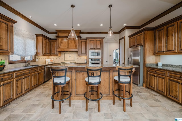 kitchen with appliances with stainless steel finishes, light stone counters, a sink, premium range hood, and a kitchen island