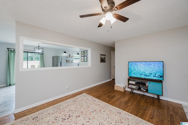 living area with baseboards, wood finished floors, and ceiling fan with notable chandelier
