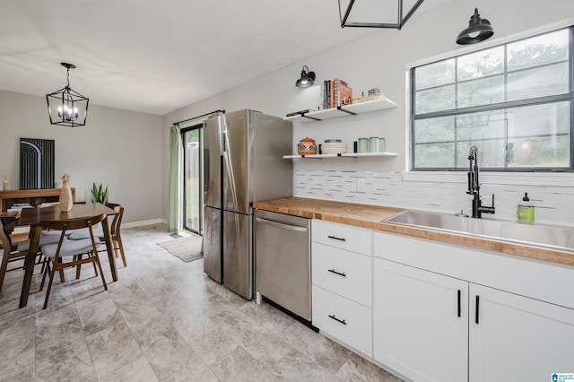 kitchen with decorative backsplash, butcher block countertops, white cabinetry, a sink, and stainless steel appliances
