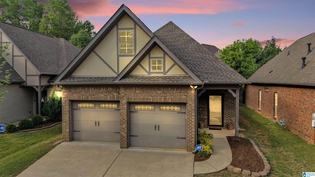 tudor home with driveway, roof with shingles, stucco siding, brick siding, and a yard