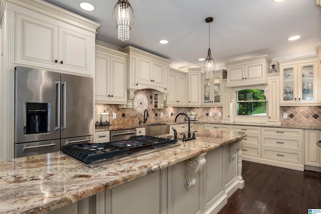 kitchen with light stone counters, stainless steel appliances, decorative backsplash, cream cabinetry, and glass insert cabinets