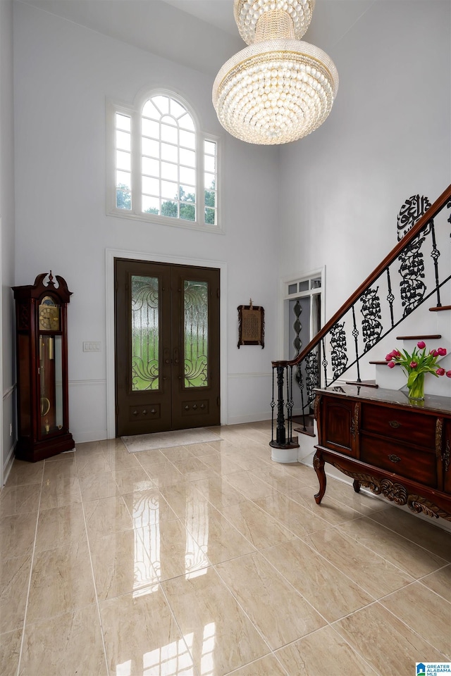 entrance foyer with marble finish floor, stairs, a high ceiling, a chandelier, and french doors