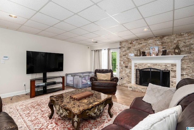 living area featuring a stone fireplace, baseboards, a drop ceiling, and wood finished floors