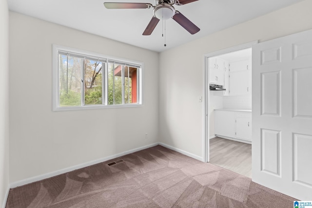 unfurnished bedroom with a ceiling fan, a walk in closet, visible vents, baseboards, and light colored carpet