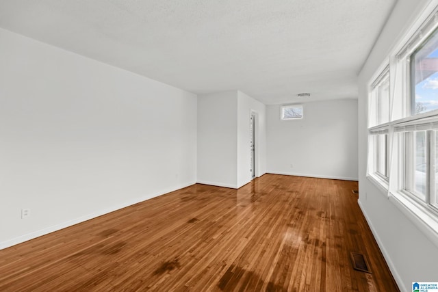 empty room featuring visible vents, hardwood / wood-style flooring, and plenty of natural light