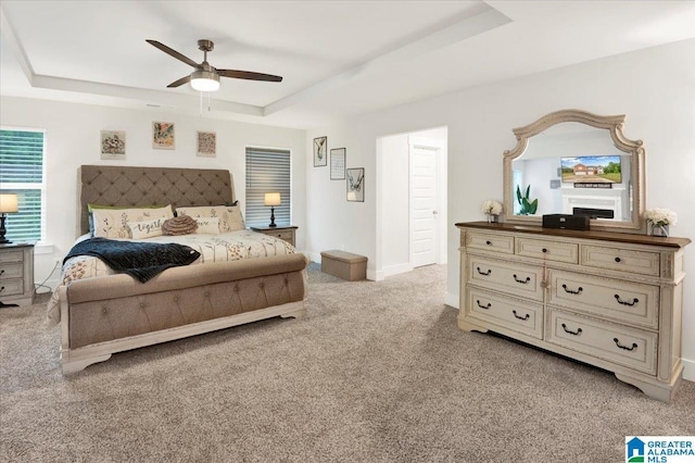 bedroom featuring ceiling fan, baseboards, light carpet, and a tray ceiling