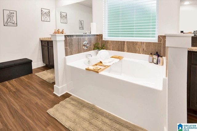 bathroom with wood finished floors, a garden tub, vanity, and baseboards