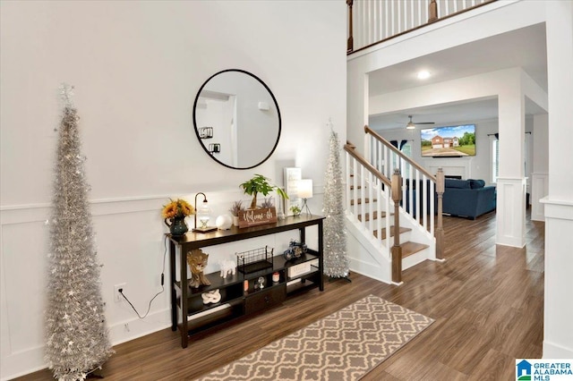 foyer featuring stairway, a ceiling fan, a decorative wall, wainscoting, and wood finished floors