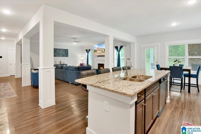 kitchen with light stone countertops, an island with sink, dishwasher, a sink, and light wood-type flooring