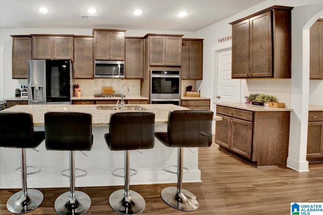 kitchen with tasteful backsplash, light stone countertops, stainless steel appliances, light wood-style floors, and a sink