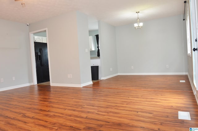 spare room with wood finished floors, a chandelier, and baseboards