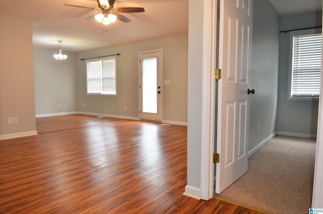 spare room featuring wood finished floors, baseboards, and ceiling fan with notable chandelier