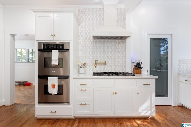 kitchen with stainless steel appliances, light countertops, ornamental molding, backsplash, and wall chimney exhaust hood