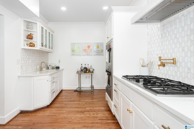 kitchen featuring decorative backsplash, glass insert cabinets, ventilation hood, light countertops, and appliances with stainless steel finishes
