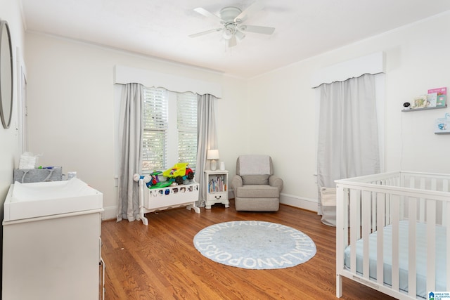 bedroom featuring wood finished floors, ceiling fan, crown molding, and a crib