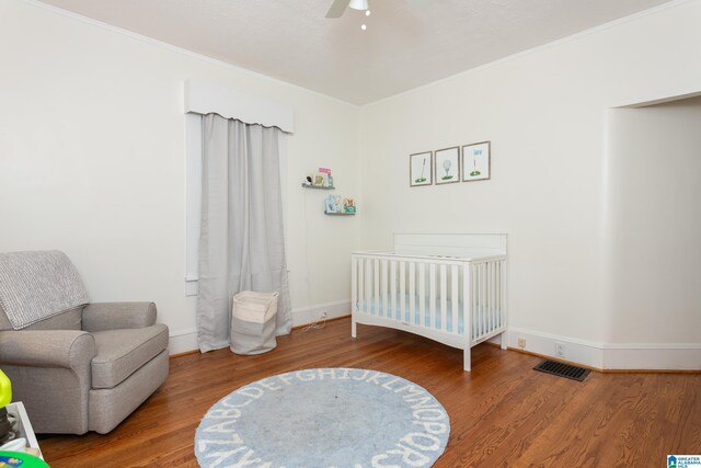 bedroom with visible vents, a crib, wood finished floors, and crown molding