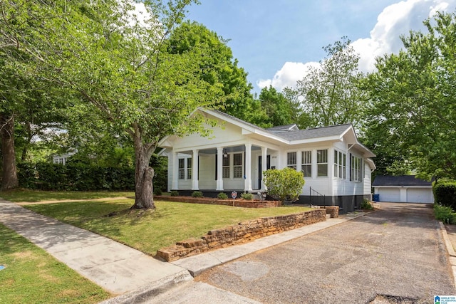view of front of property featuring an outdoor structure, a detached garage, a front yard, and a shingled roof