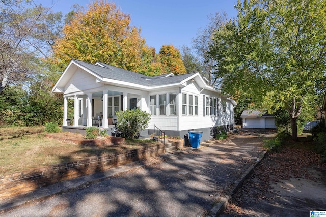 view of property exterior featuring covered porch, a shingled roof, an outbuilding, and driveway