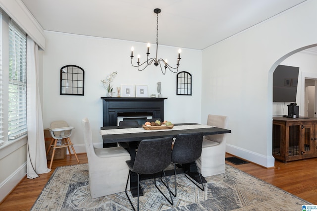 dining room featuring arched walkways, a notable chandelier, wood finished floors, and baseboards