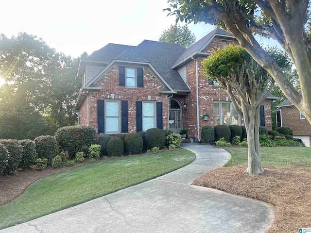 traditional-style house with roof with shingles, a front yard, and brick siding