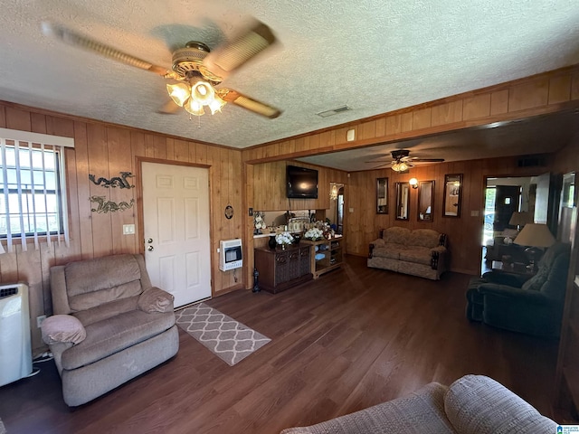 living area featuring dark wood finished floors, heating unit, wood walls, a ceiling fan, and a textured ceiling