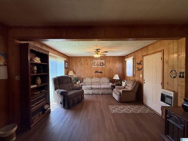 living room featuring a textured ceiling, ceiling fan, dark wood-style flooring, wooden walls, and heating unit