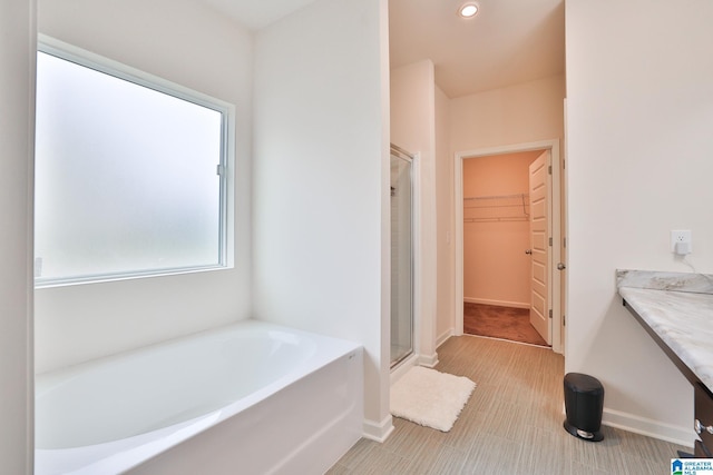 full bath featuring a spacious closet, a shower stall, a bath, and baseboards