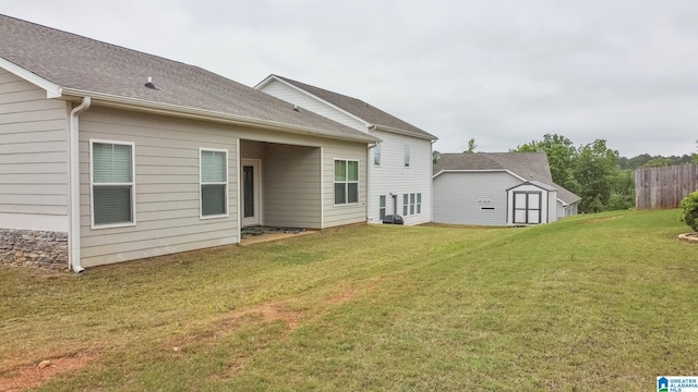 rear view of house featuring an outbuilding, a yard, roof with shingles, a storage unit, and fence
