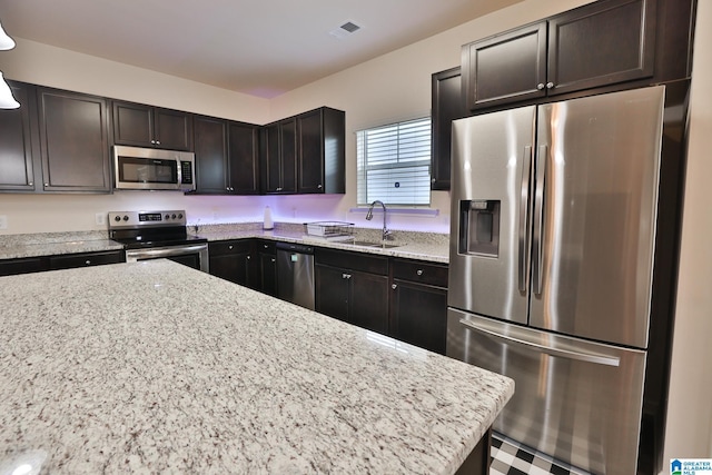 kitchen with light stone countertops, stainless steel appliances, dark brown cabinets, a sink, and visible vents