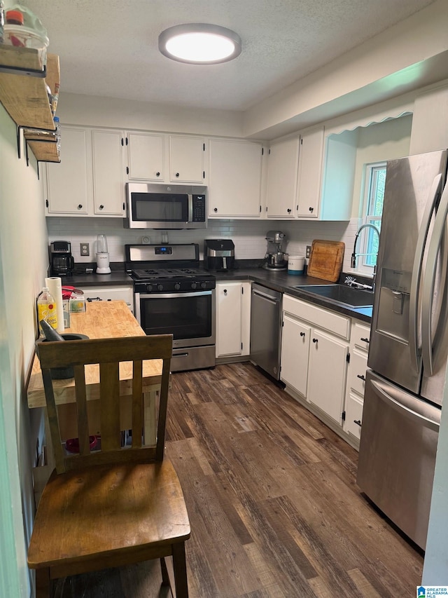 kitchen with white cabinetry, a sink, appliances with stainless steel finishes, dark countertops, and dark wood finished floors