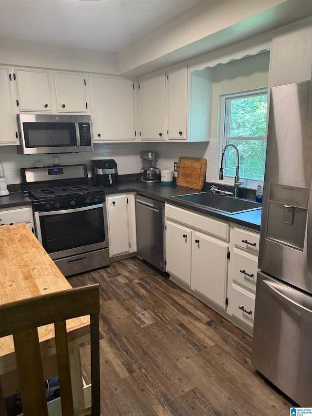 kitchen featuring appliances with stainless steel finishes, dark countertops, dark wood-style flooring, a sink, and white cabinetry