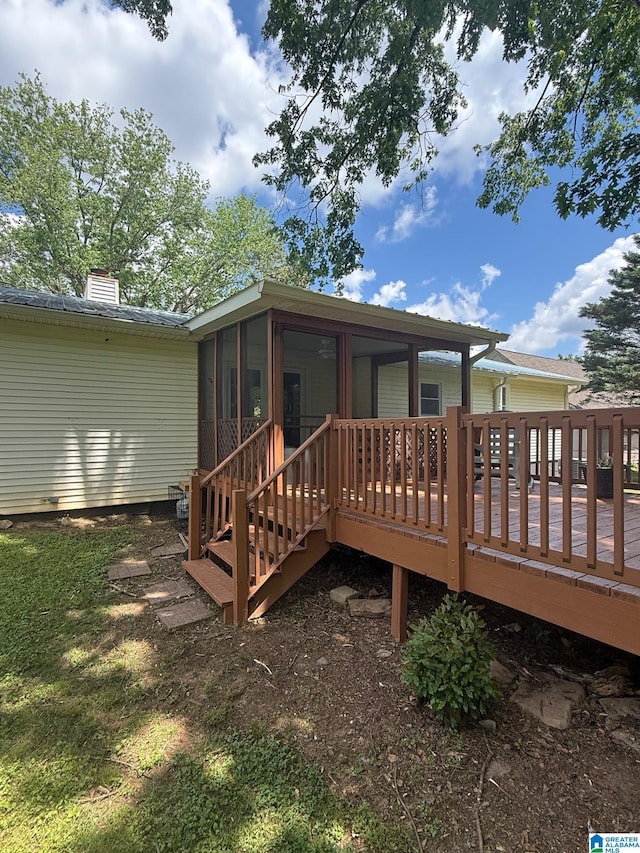 back of property with a chimney, a wooden deck, and a sunroom