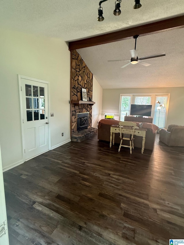 living room featuring lofted ceiling with beams, ceiling fan, a stone fireplace, a textured ceiling, and wood finished floors