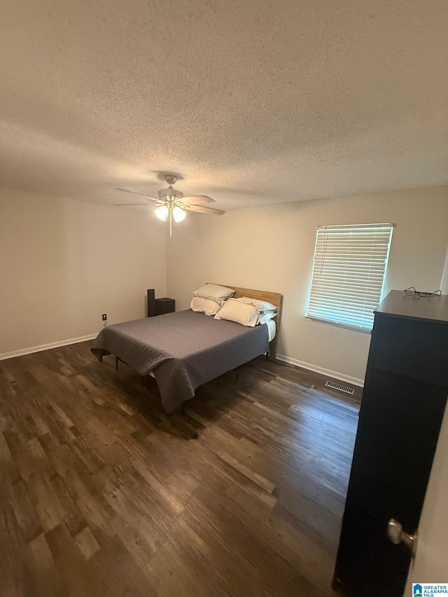 bedroom featuring dark wood finished floors, visible vents, a ceiling fan, and a textured ceiling
