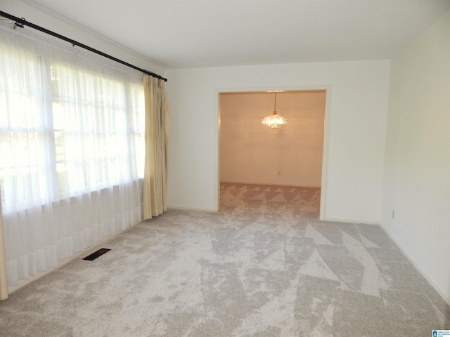 unfurnished room featuring carpet flooring, visible vents, and an inviting chandelier