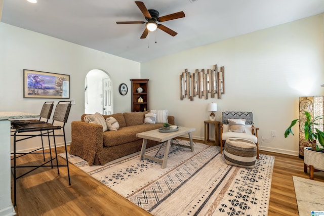 living area with baseboards, a ceiling fan, arched walkways, and wood finished floors