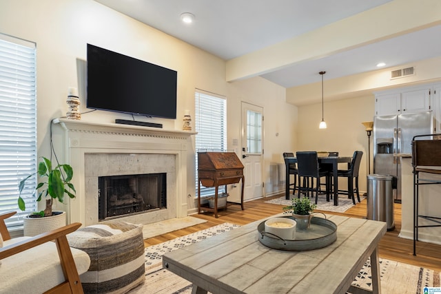 living area featuring beam ceiling, light wood finished floors, recessed lighting, a high end fireplace, and visible vents