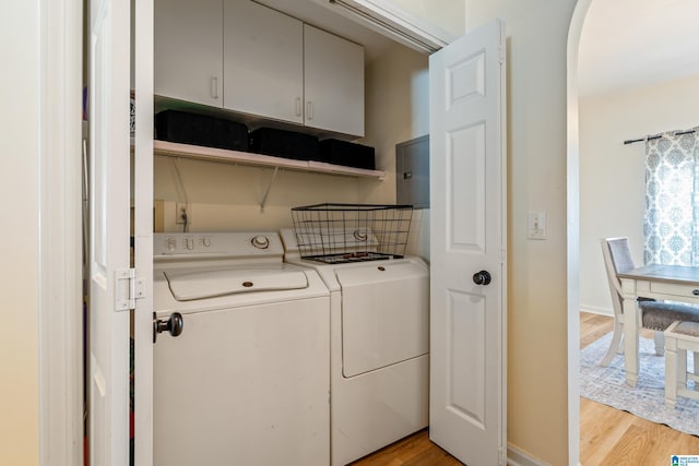 washroom featuring cabinet space, arched walkways, baseboards, light wood-type flooring, and washer and clothes dryer
