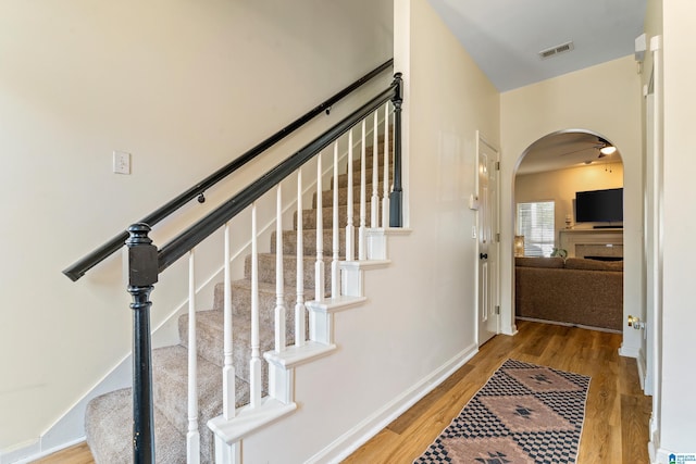 stairs with visible vents, arched walkways, baseboards, and wood finished floors