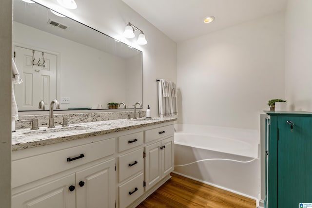 bathroom with a sink, double vanity, wood finished floors, and visible vents